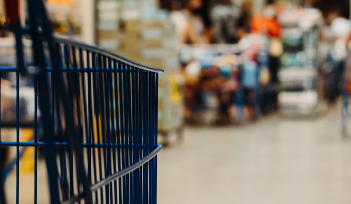 Carrinho de compras em primeiro plano dentro de uma loja com clientes ao fundo