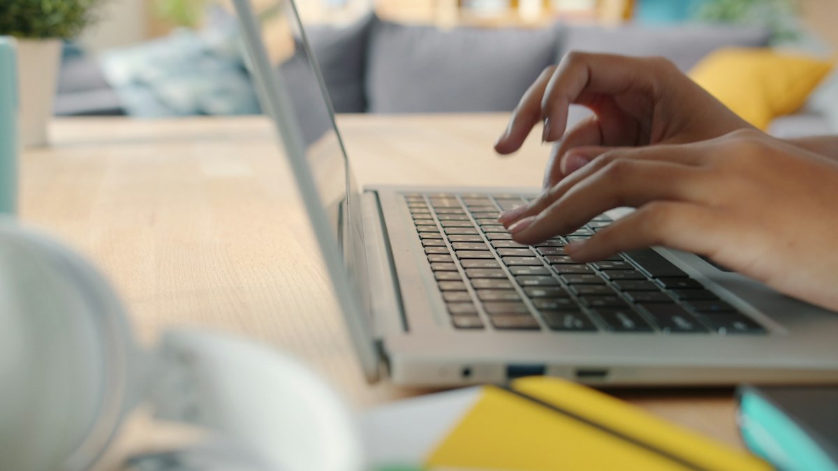 Mãos digitando em um notebook sobre a mesa de um escritório em casa